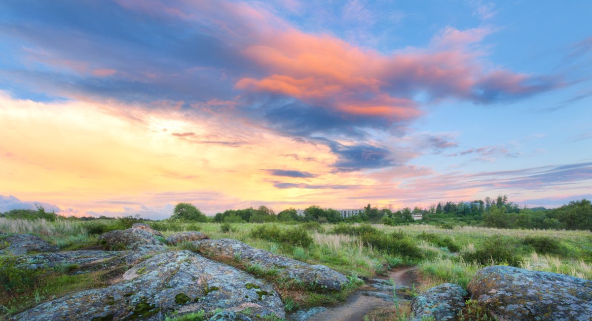 Colorful summer landscape with big stones, green grass, walkway and amazing sky with multicolored clouds at sunset. Nature background. Rocks in the beautiful steppe in the evening. Park in Ukraine